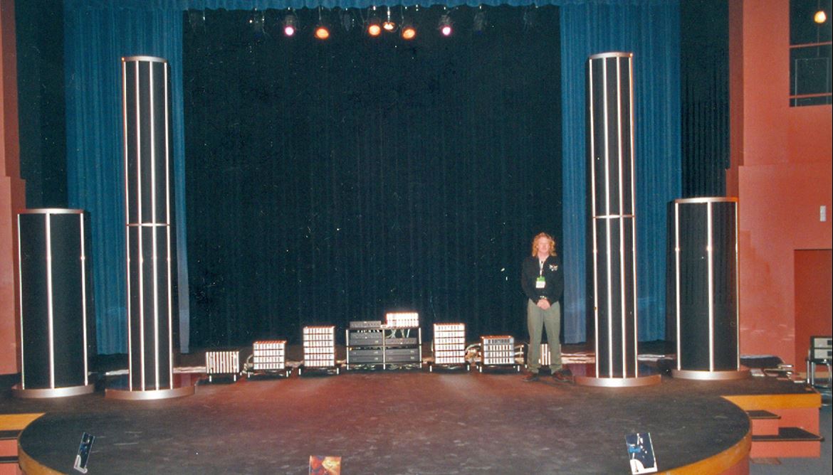 Robert Smith posa junto a uma das colunas de som, com os seus longos cabelos louros